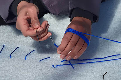 still from 'solitary stitches: sand, snow, soil' by Elham Fatapour depicts hands sewing thread into the snow