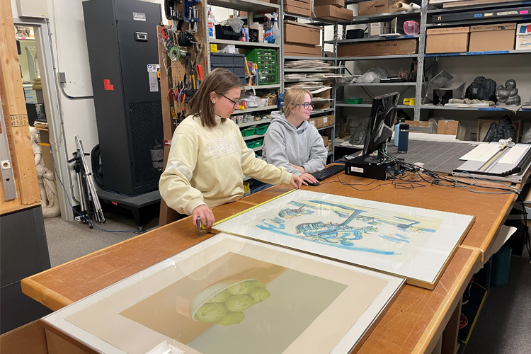 Collections Assistant Emily and collections volunteer Kath measure an artwork in the vault